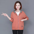 A woman wearing a peach-coloured zip-up hoodie with a black and white gingham lined hood and front patch pockets.