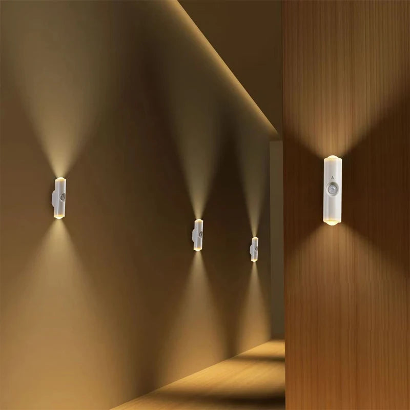 Sleek white, rechargeable LED wall lamps with motion sensors, casting warm, upward and downward beams along a hallway.
