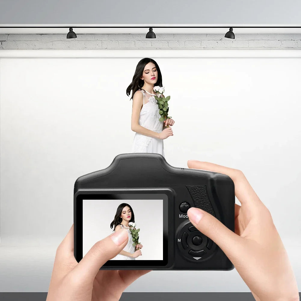 Black plastic digital camera with a rear screen held in two hands, showing a live preview of a woman with white roses.
