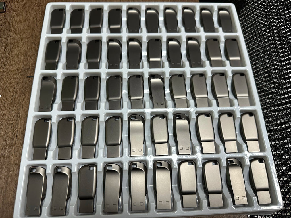 A bulk tray of sleek, metallic dark grey USB 3.0 flash drives with a curved, compact design and keyhole attachment.