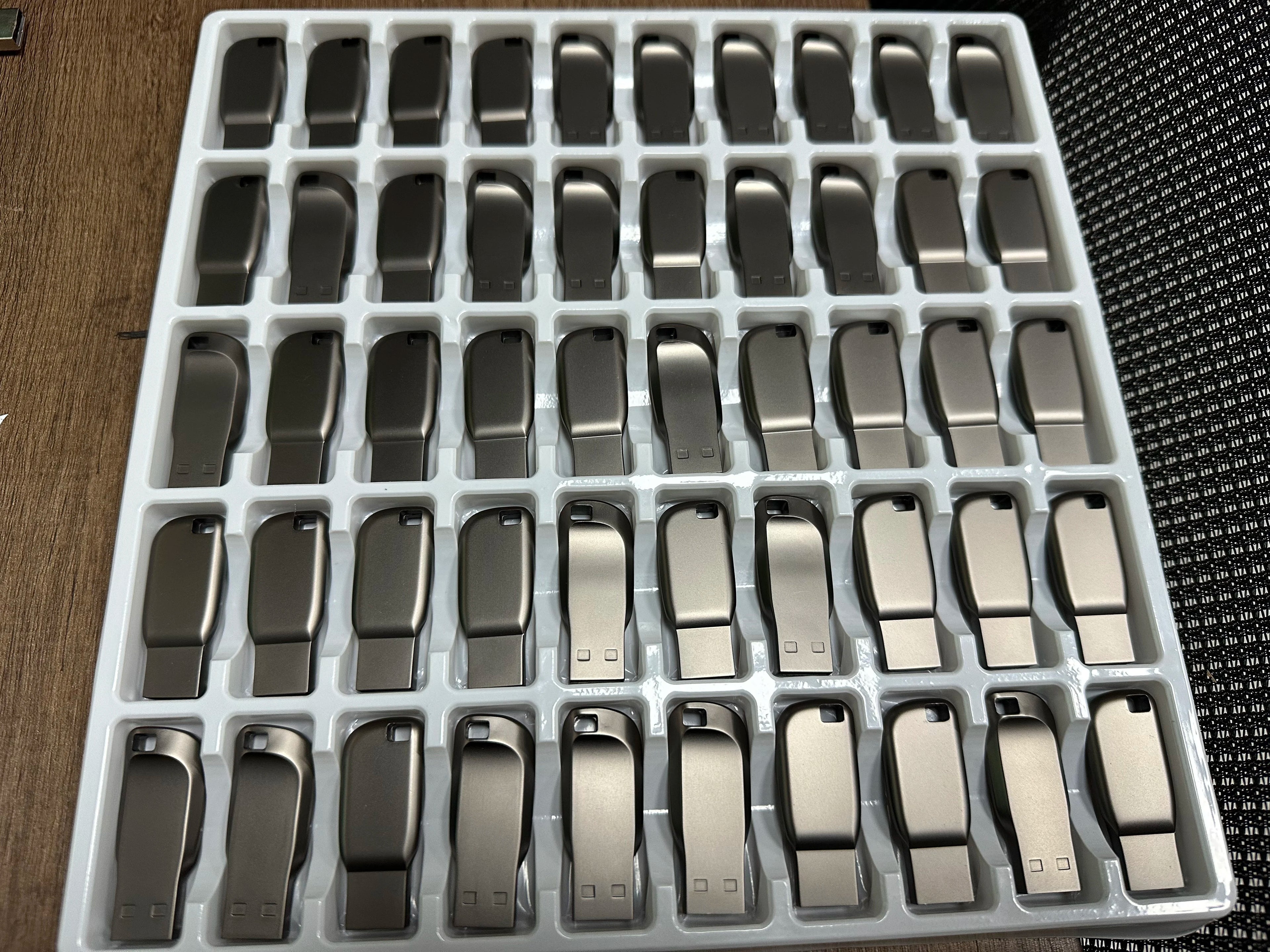 A bulk tray of sleek, metallic dark grey USB 3.0 flash drives with a curved, compact design and keyhole attachment.
