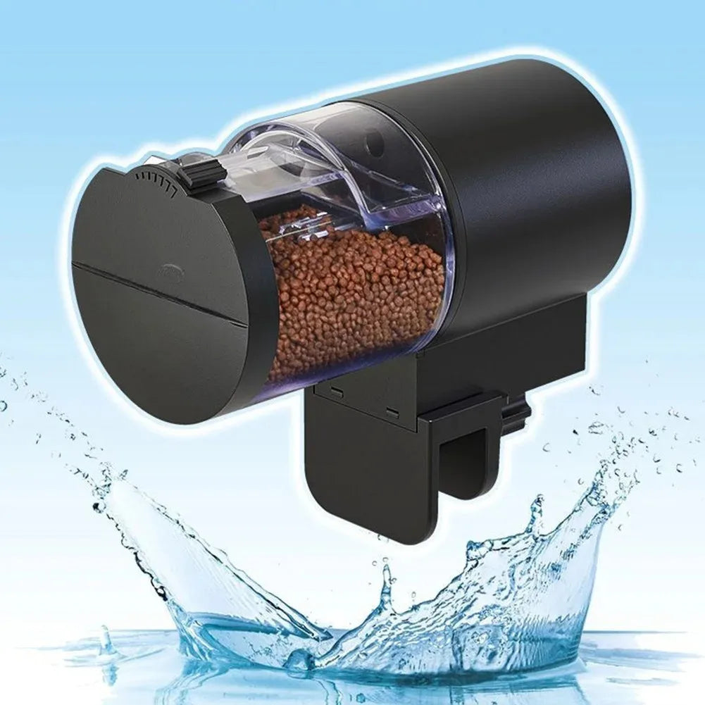 Black automatic fish feeder with a clear, pellet-filled container and a sturdy mount, shown above splashing water.