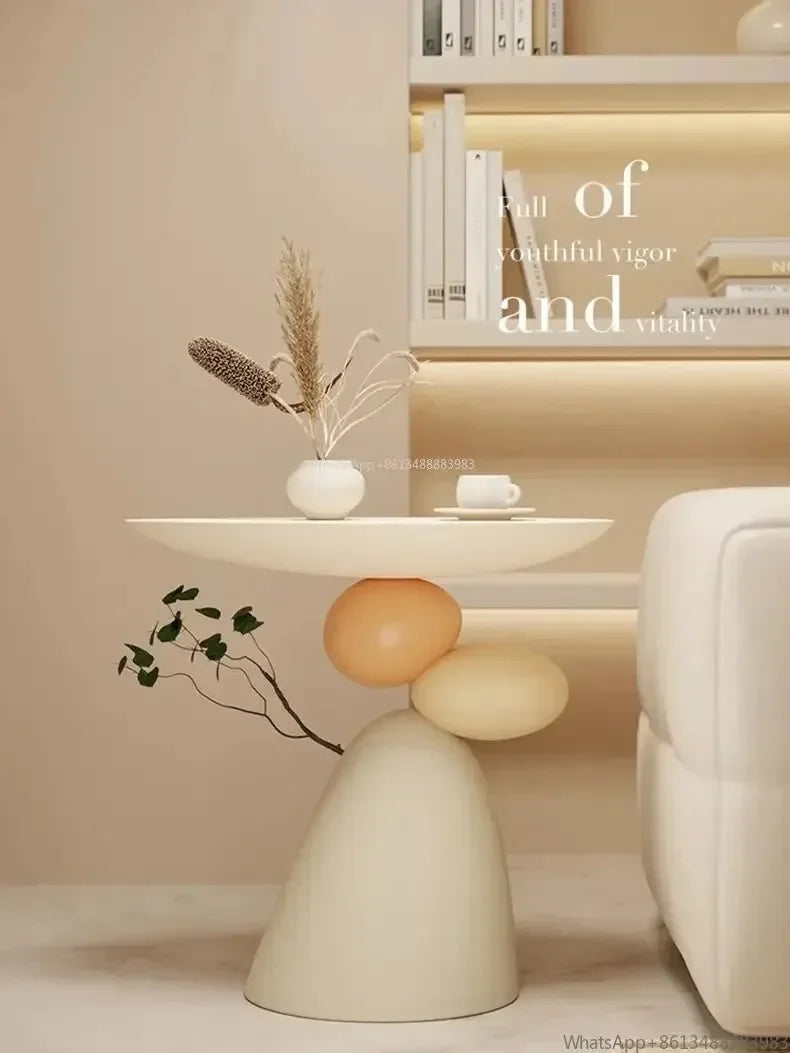 Minimalist cream-coloured side table featuring a smooth round top and a unique base of stacked, pebble-shaped forms.