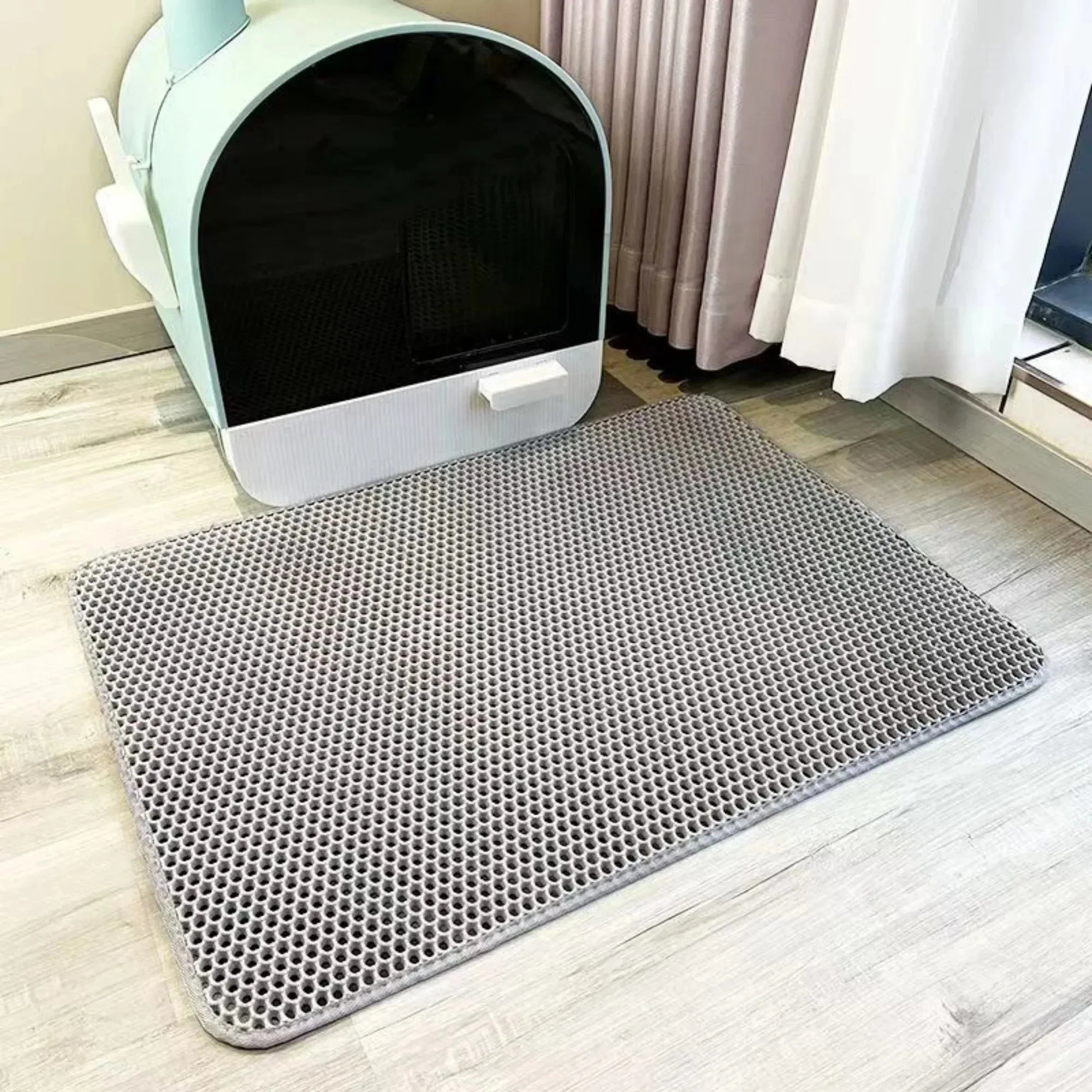 Grey, rectangular, waterproof cat litter mat with a textured honeycomb surface, placed on a wooden floor.