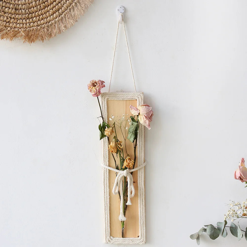 Bohemian wall hanging featuring a slim wooden plaque framed with cream rope, holding a bouquet of dried pink roses.