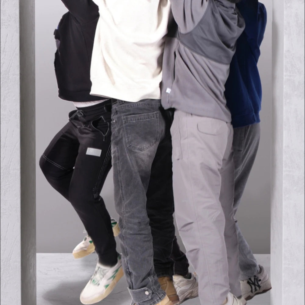 Four people standing in a row, wearing hoodies, jeans, and joggers in black, white, grey, and navy with trainers.