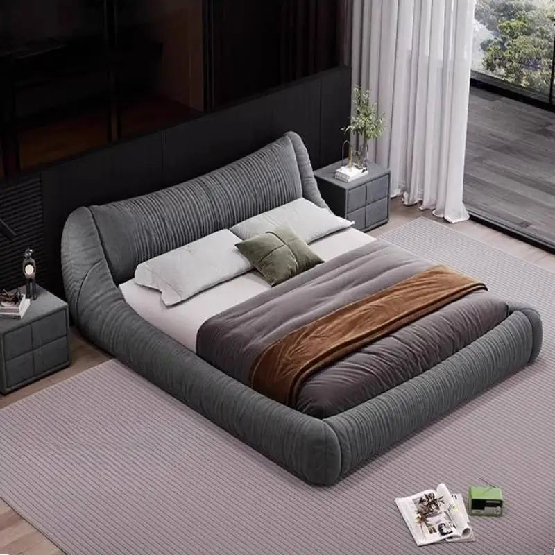A charcoal grey, tufted fabric bed frame with a modern, low-profile design and rounded edges in a contemporary bedroom.
