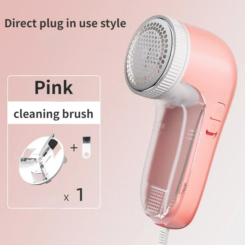 A pink electric fabric shaver with a transparent lint bin, a replacement blade, and a small cleaning brush.