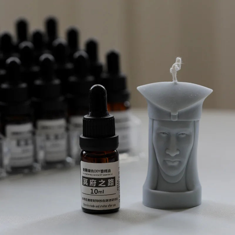 Grey wax candle shaped like a historical figure’s head, positioned next to a 10ml amber glass essential oil dropper.