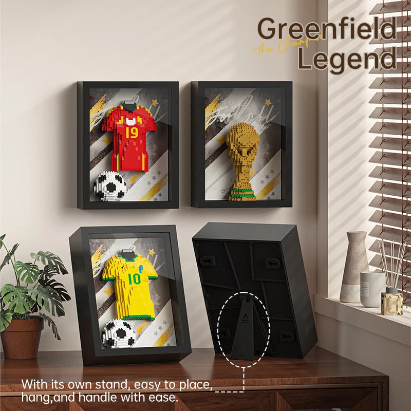 Four black shadow box frames displaying 3D brick-built football shirts, a trophy, and footballs on a wooden desk.