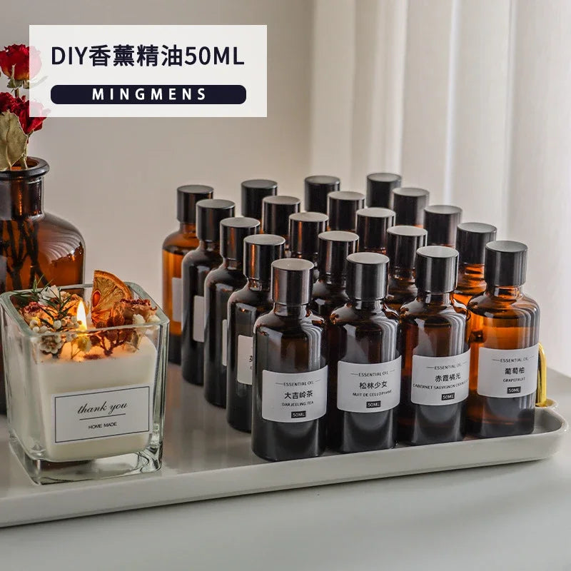 Set of 50ml amber glass essential oil bottles with white labels on a white tray, next to a scented candle.