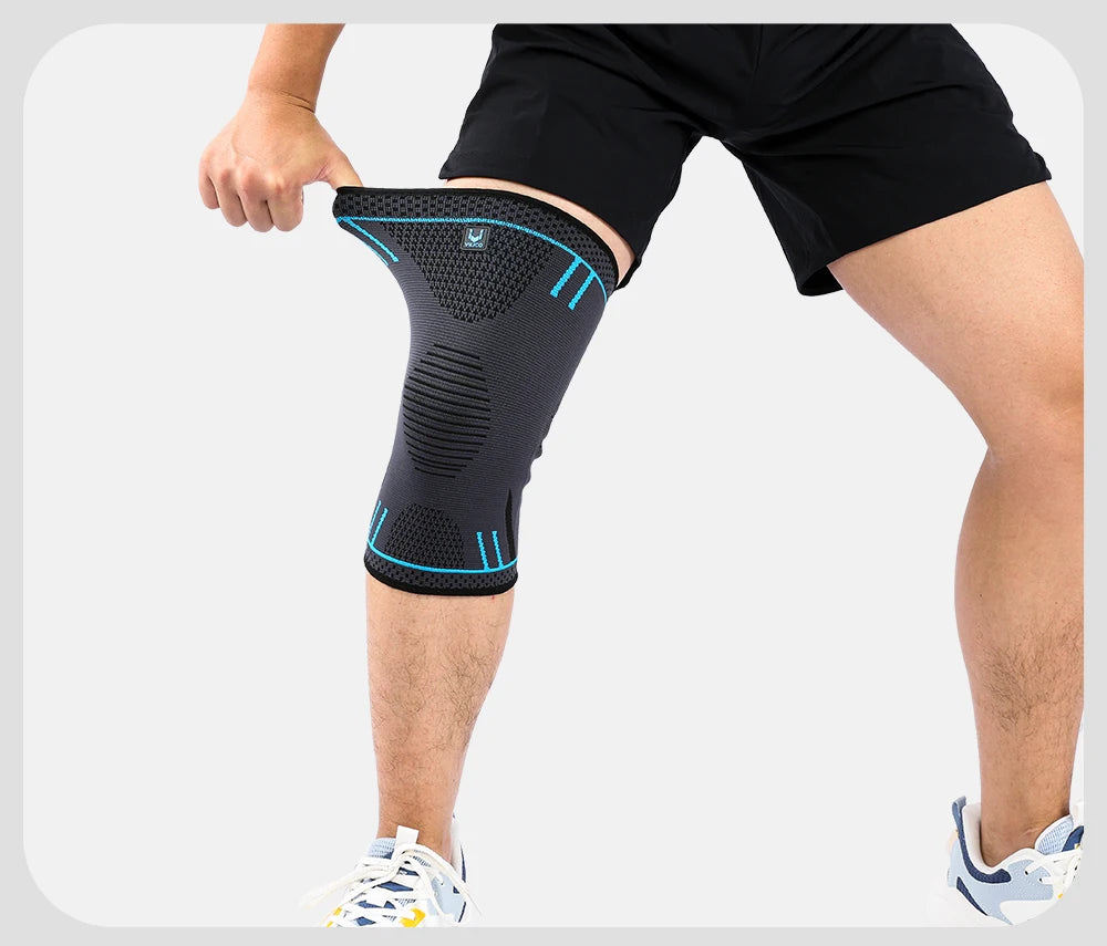 Grey and black compression knee support sleeve with blue trim, worn on a leg with black shorts and trainers.