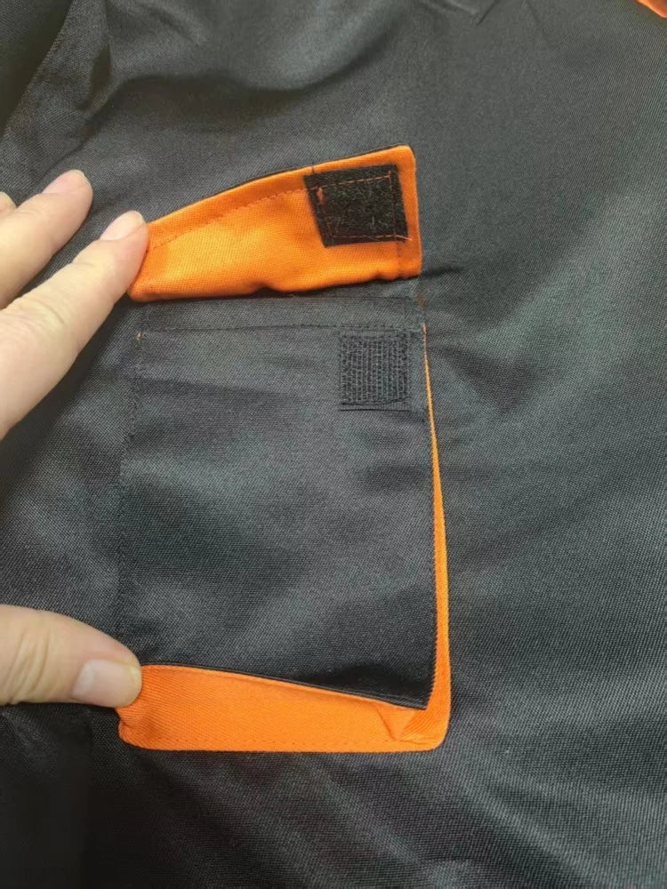 Close-up of black heavy-duty mechanic coveralls with a contrasting orange pocket flap and hook-and-loop fastening.