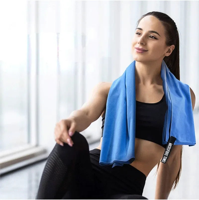 A woman in black gym wear wearing a bright blue microfibre gym towel around her neck.