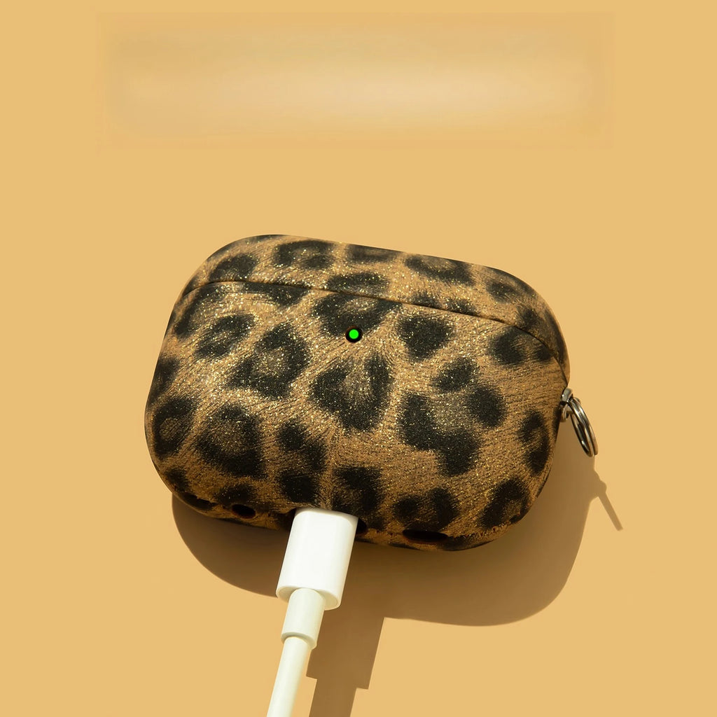 Gold glitter leopard print AirPods Pro case being charged with a white cable against a tan background.