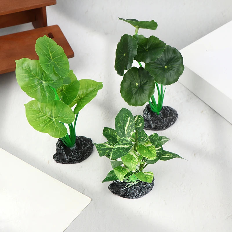 Three artificial aquarium plants with sturdy, dark, rock-like bases set against a light background.