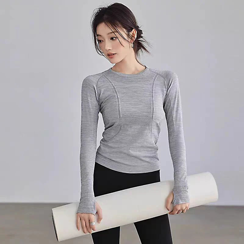 Woman wearing a grey, long-sleeved seamless gym top with thumbholes and athletic contour detailing.