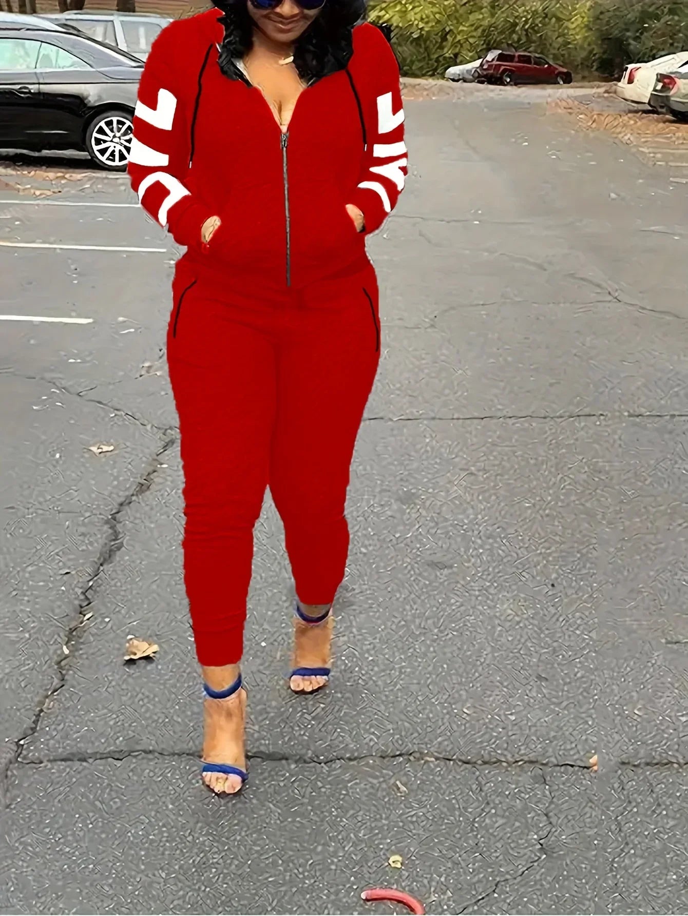 Woman wearing a red zip-up hooded tracksuit with white sleeve stripes, styled with blue high-heeled sandals.