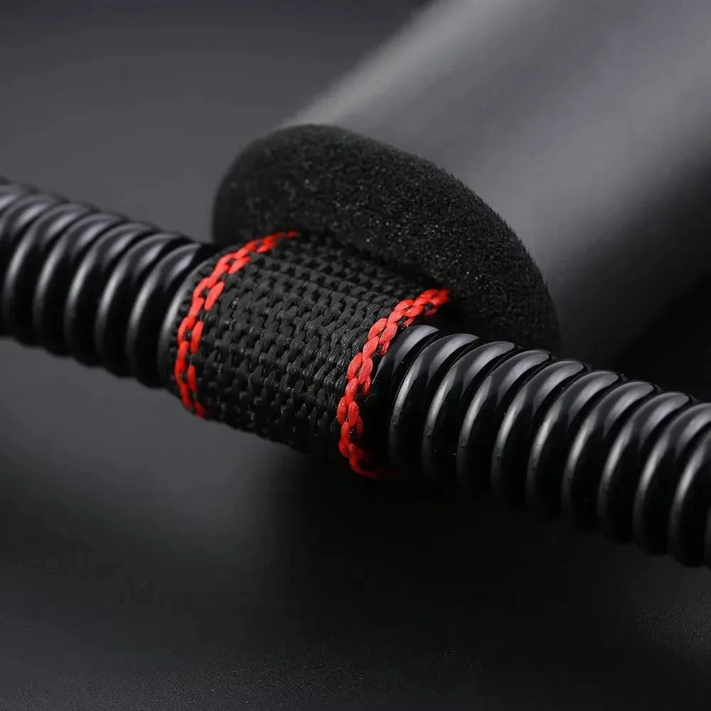 Close-up of a black exercise spring with a central foam grip and textured strap featuring red contrast stitching.