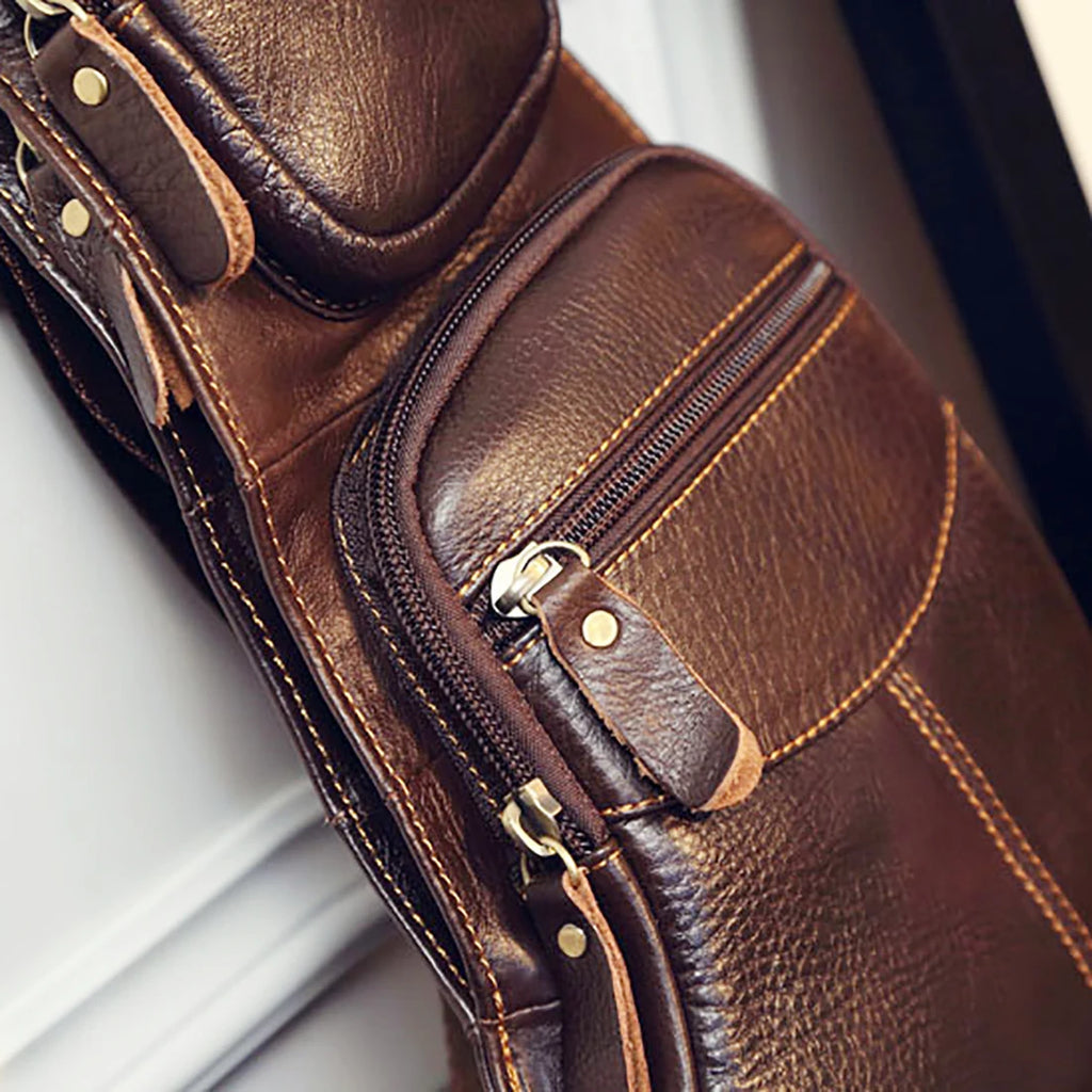 Dark brown pebbled leather men's crossbody sling bag with external zipped pockets and metal stud detailing.