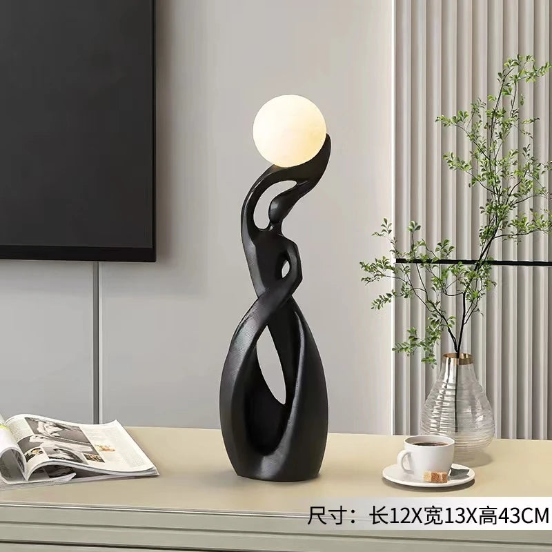 Contemporary black resin abstract figure ornament, featuring a smooth, curved design holding an illuminated sphere.