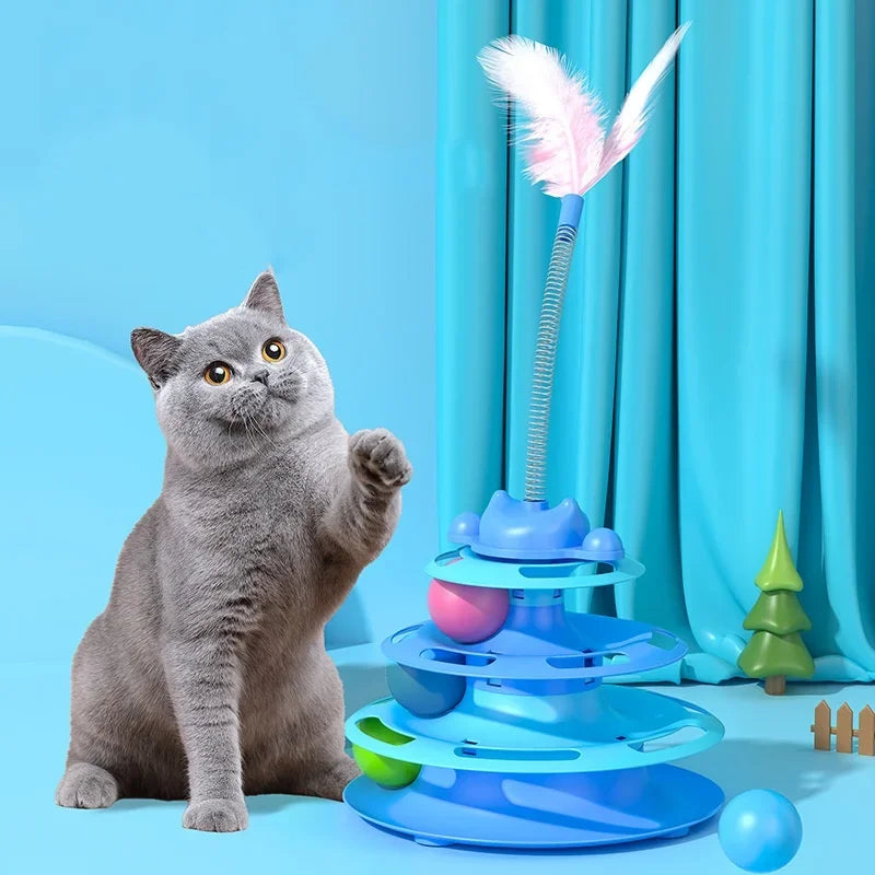 Grey cat playing with a blue tiered interactive turntable toy featuring colourful balls and a springy feather wand.