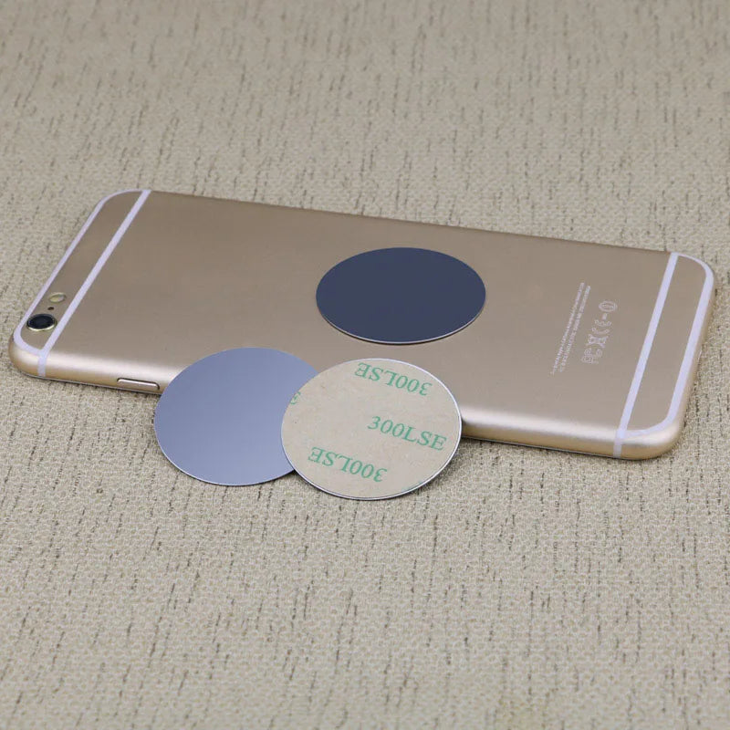 Three circular adhesive metal plates, two grey and one with a tan backing, displayed with a gold smartphone.