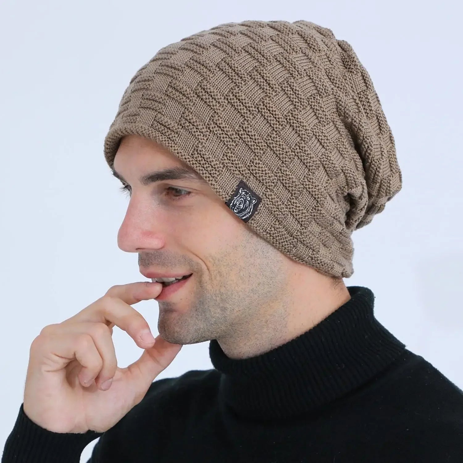 A man wearing a tan, textured cable-knit slouchy beanie hat against a white background.