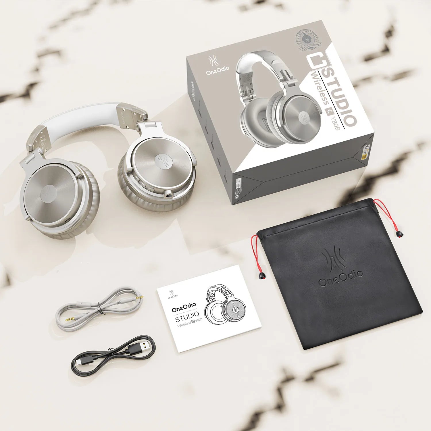 Silver and white wireless over-ear headphones with microphone, shown with cables, manual, storage bag and packaging.