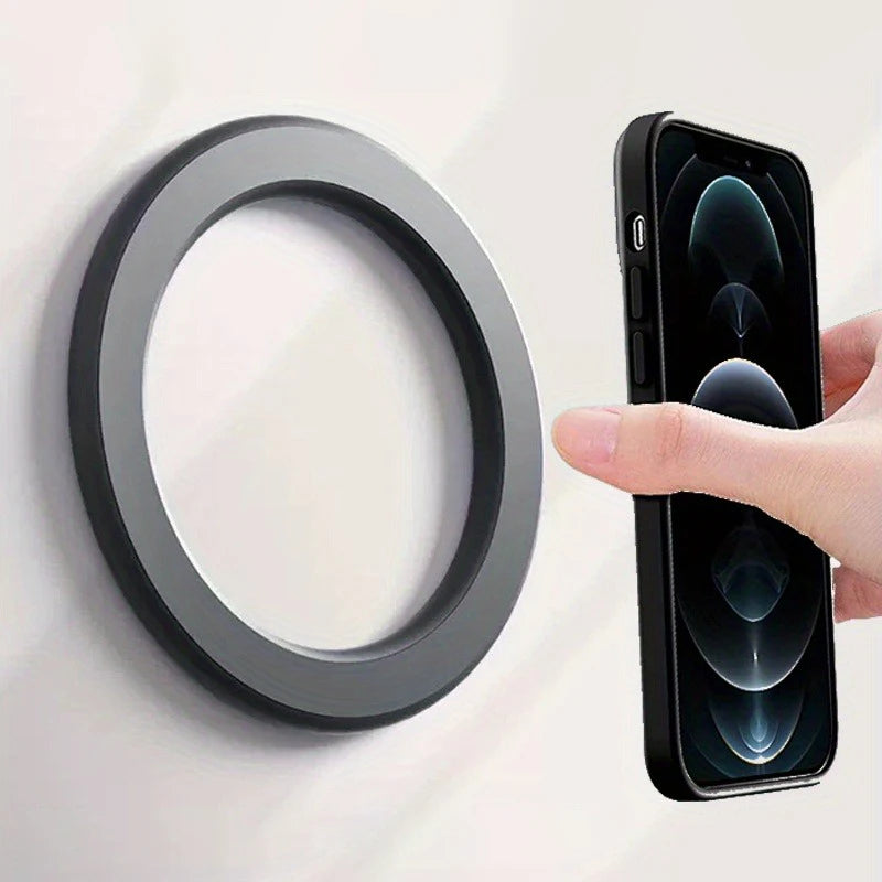 A round, matte black magnetic wall mount held by a hand with a black smartphone.