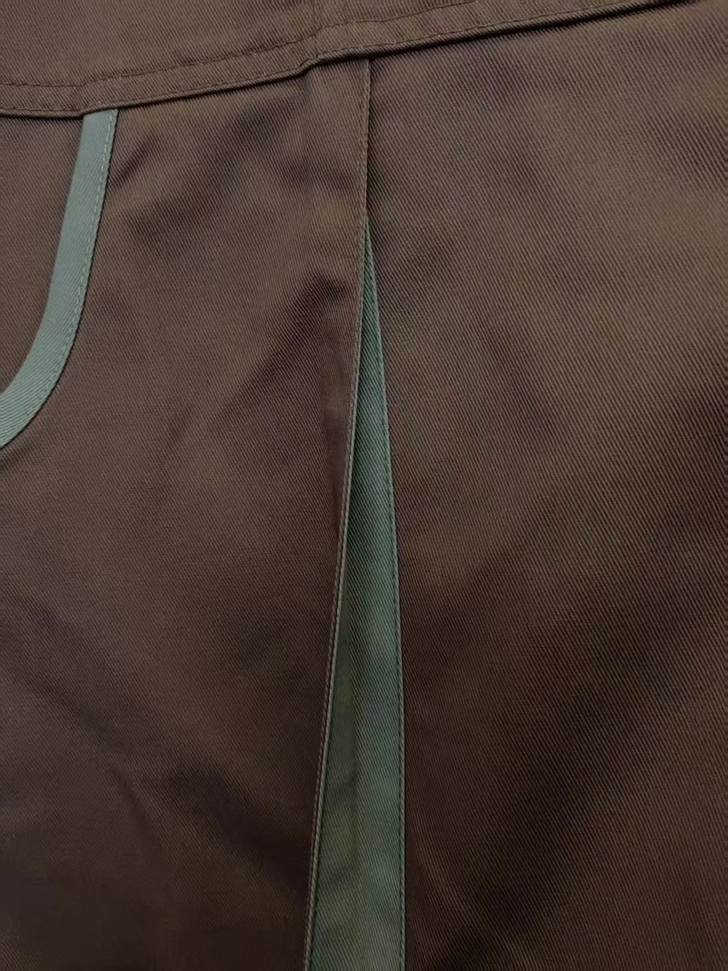 Close-up of heavy-duty brown cotton drill coveralls with reinforced seams and grey contrast detailing.
