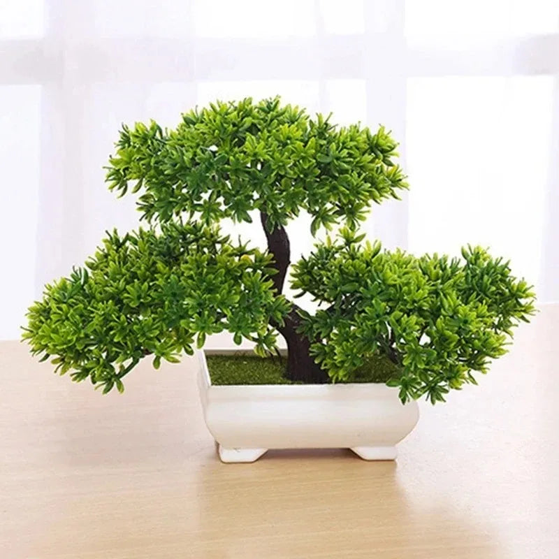 Artificial bonsai tree with vibrant green leaves and a dark trunk in a small, rectangular white pot on a table.