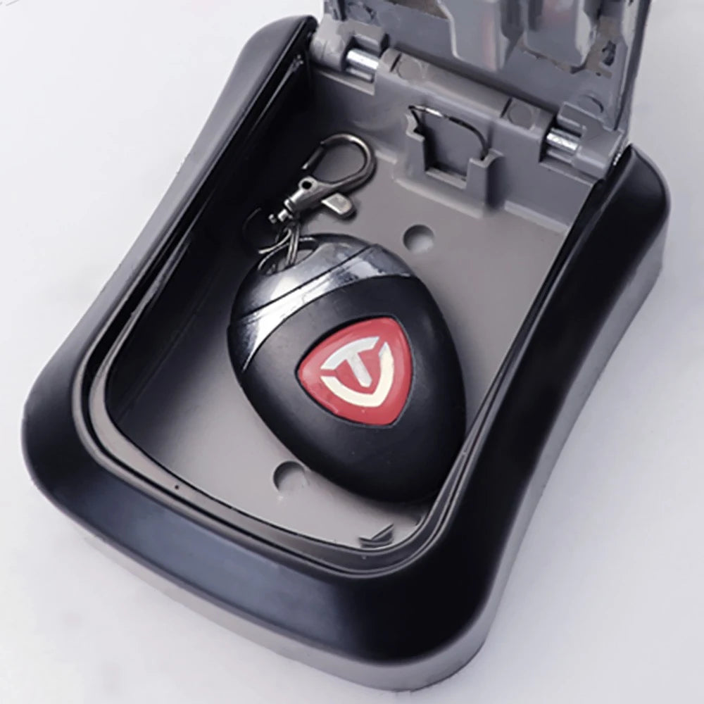 A black wall-mounted key lock box open, containing a black key fob with a red and white 'T' logo.