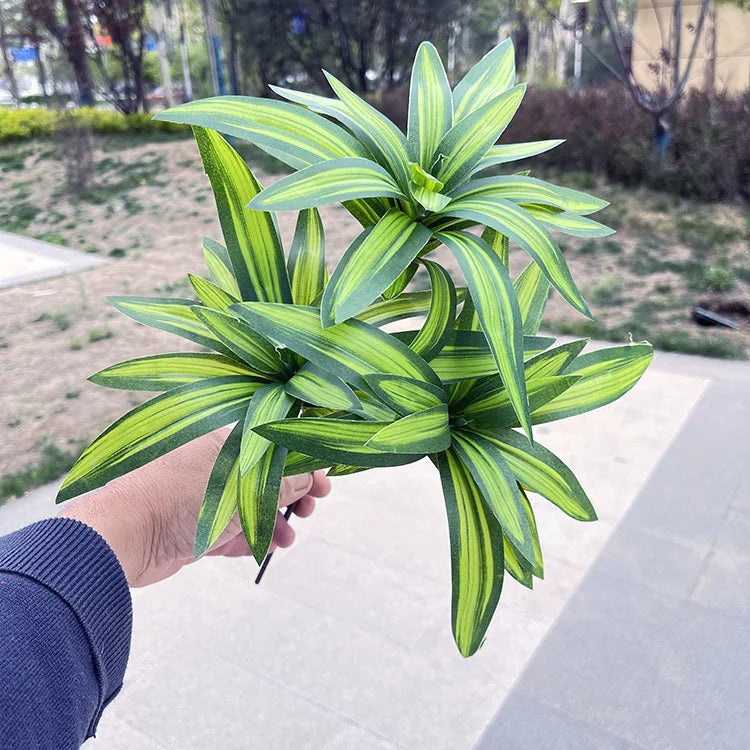 A hand holds a bunch of artificial lily branches with long, pointed green and yellow variegated leaves.