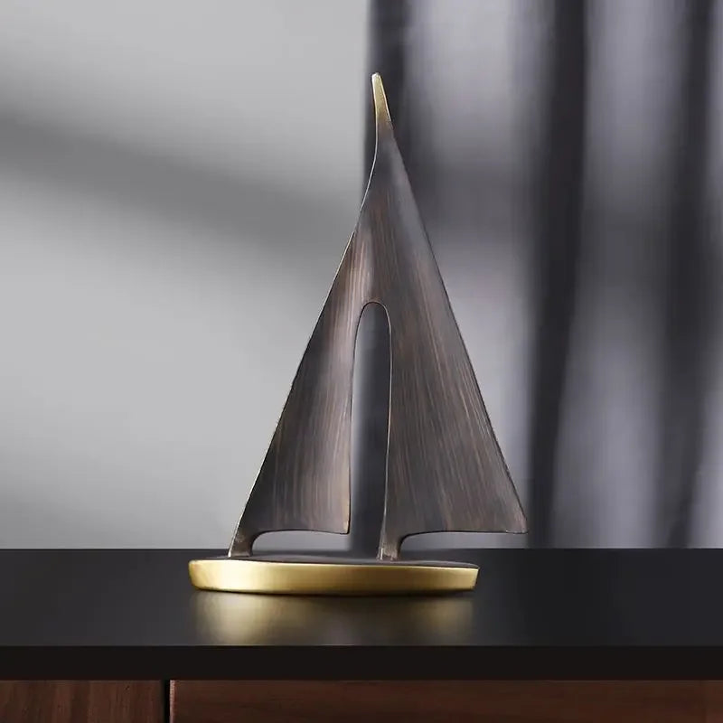 Minimalist sailboat ornament with dark, brushed-finish sails and a smooth, gold-toned base on a dark surface.