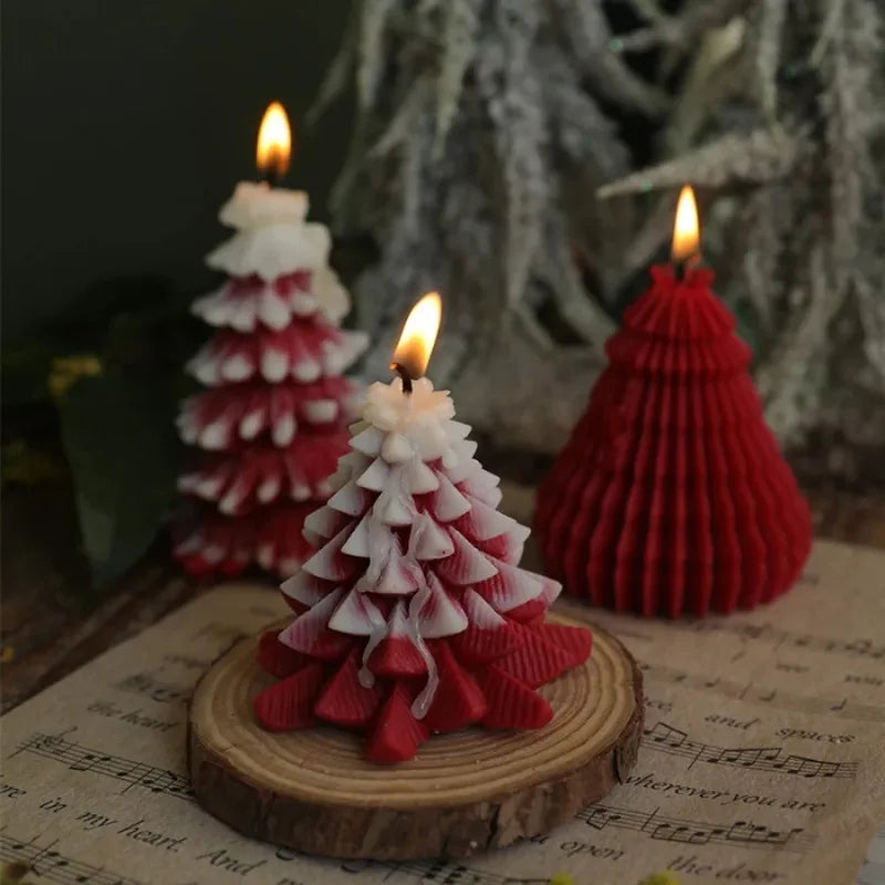 Three festive, lit Christmas tree-shaped candles in red and white on a wooden slice coaster.