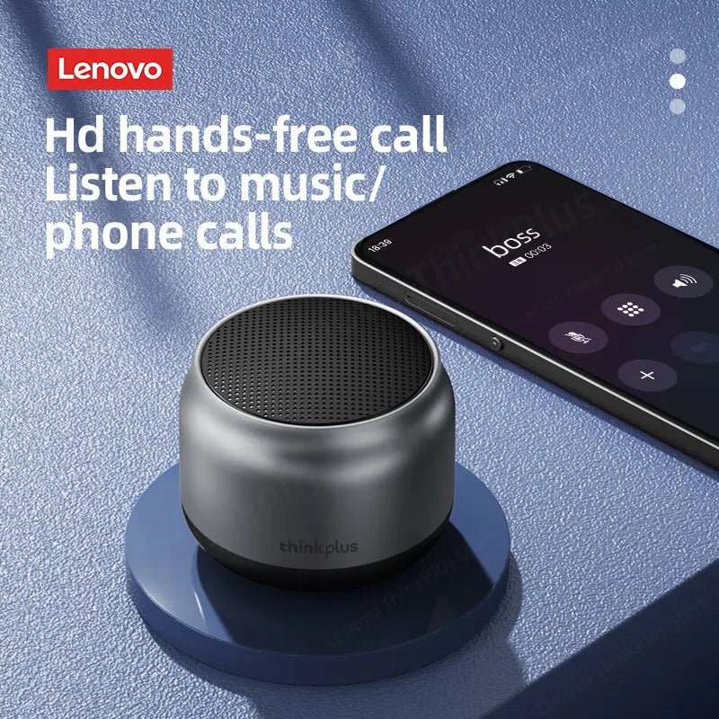 Small, metallic grey portable Bluetooth speaker with a black top grille, shown next to a smartphone.