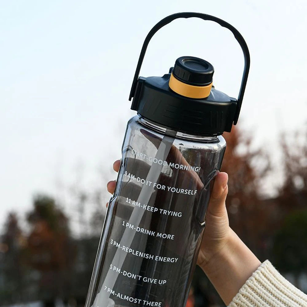 Black motivational water bottle with hourly time markers and a black carry handle, held against an outdoor background.