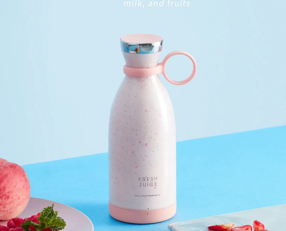 A portable, pale pink blender bottle filled with a smoothie, featuring a metallic cap and silicone carrying loop.