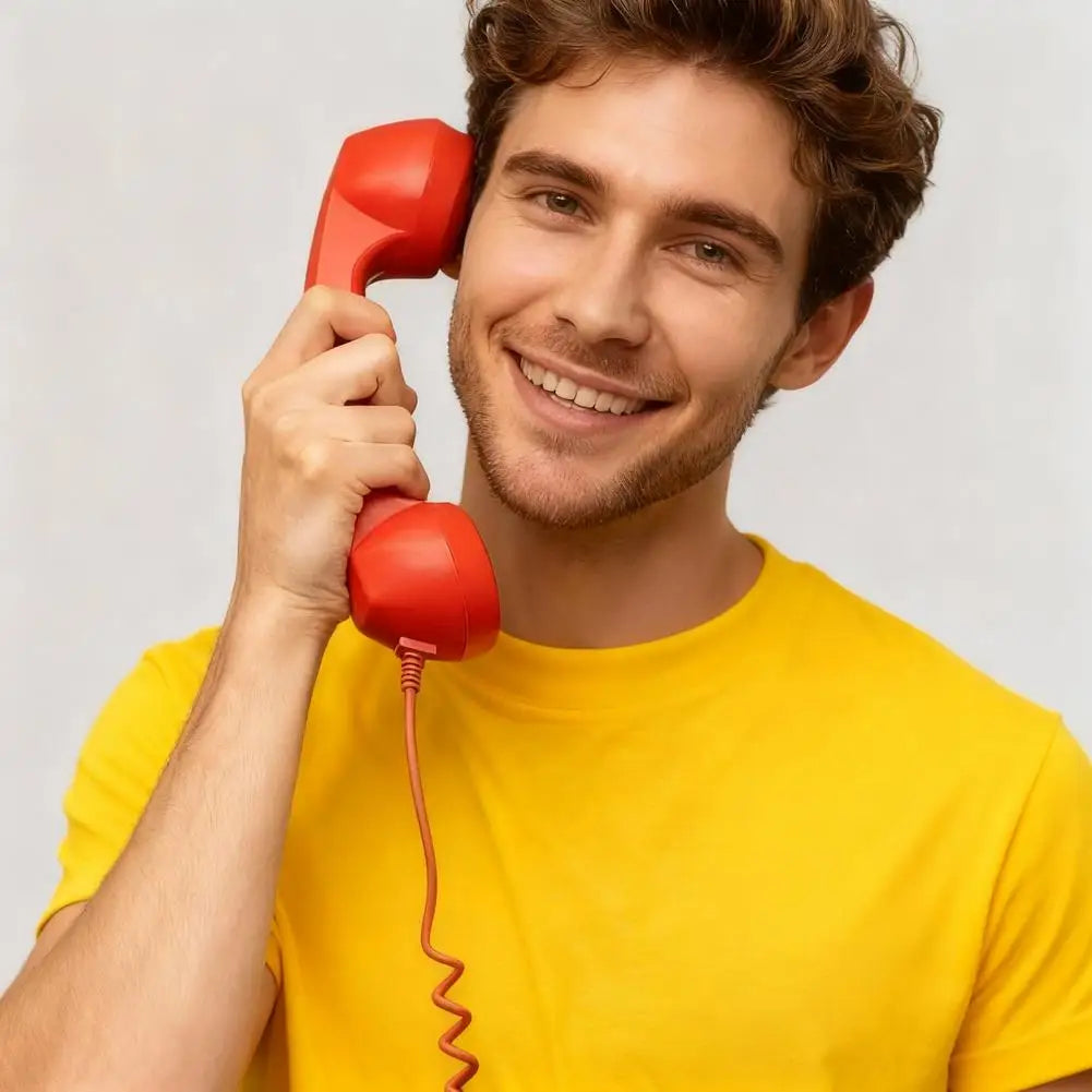 Smiling man in a yellow T-shirt holding a retro-style bright red corded telephone handset to his ear.