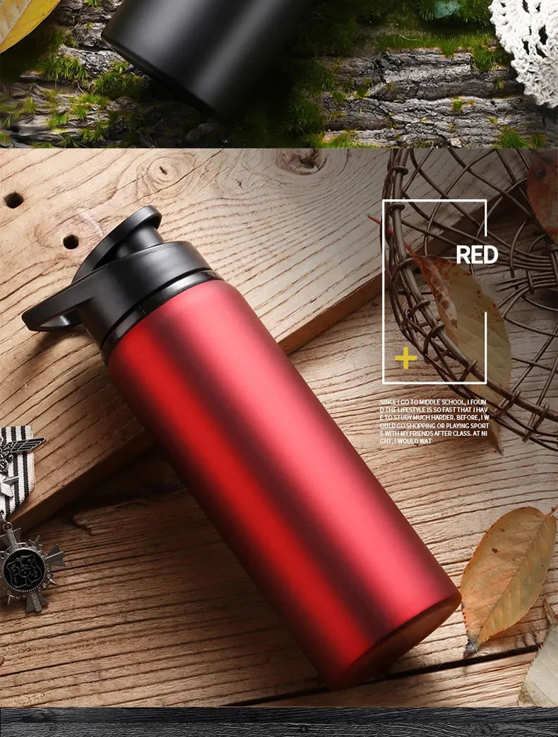 Matte red reusable water bottle with a black screw-top lid and carry handle, set on a rustic wooden table.