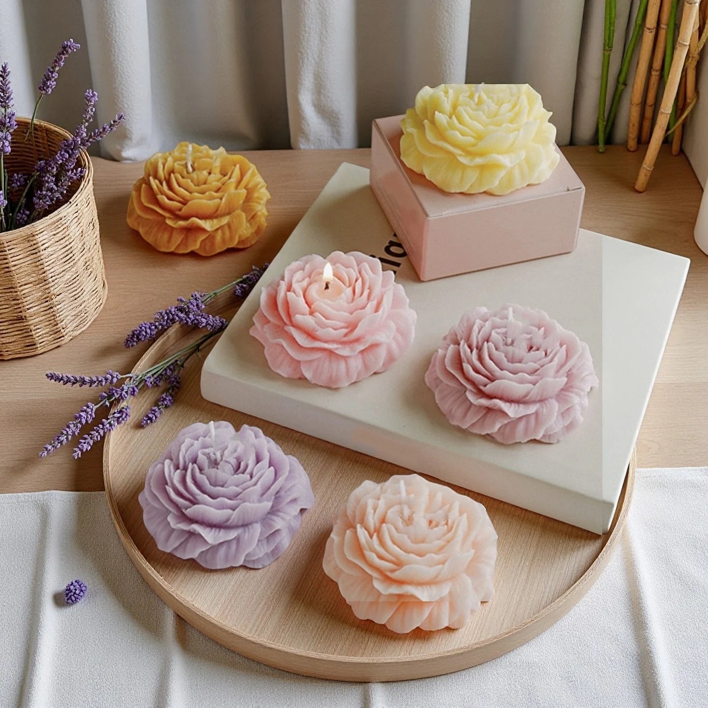 Collection of pastel-coloured, peony-shaped decorative candles arranged on a wooden tray with sprigs of lavender.