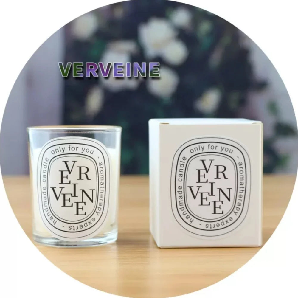 Verveine scented handmade aromatherapy candle in a glass votive with matching white gift box on a wooden surface.