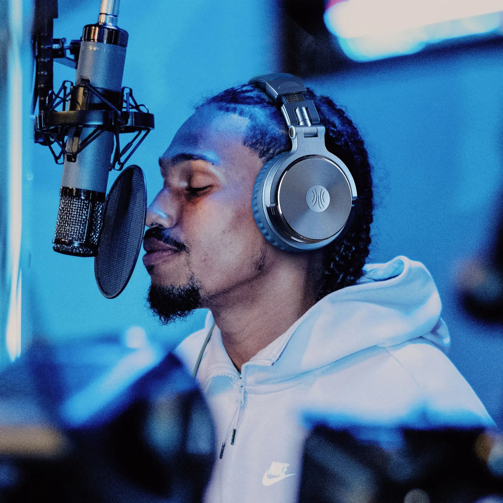 A man wearing sleek, silver professional studio headphones in a recording booth with a condenser microphone.