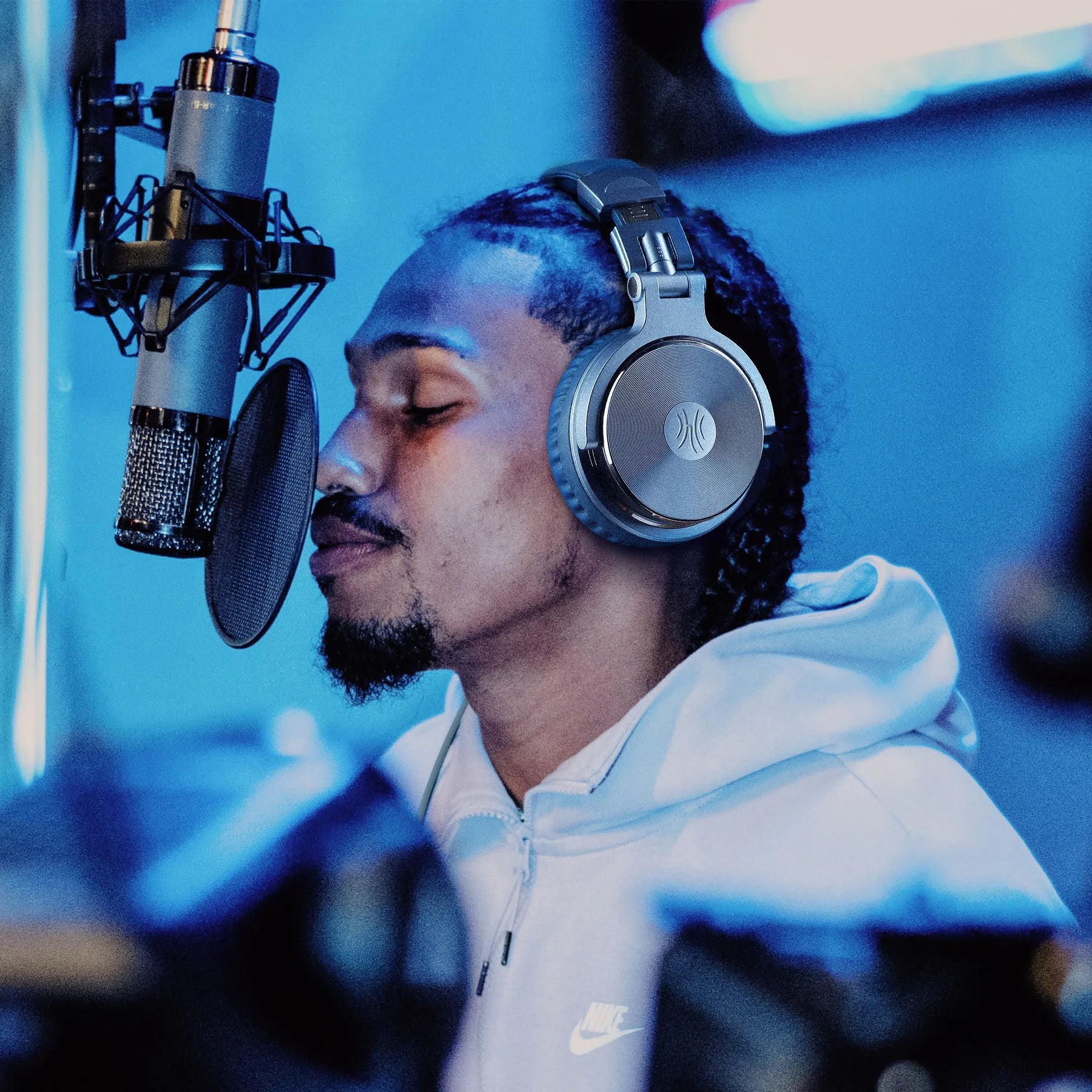 A man wearing sleek, silver professional studio headphones in a recording booth with a condenser microphone.