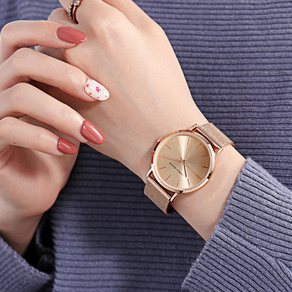 Minimalist rose gold women's watch with round face and mesh strap worn on wrist.