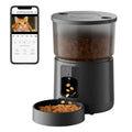 Black automatic pet feeder with a translucent food hopper, camera, and a connected smartphone app displaying a cat.