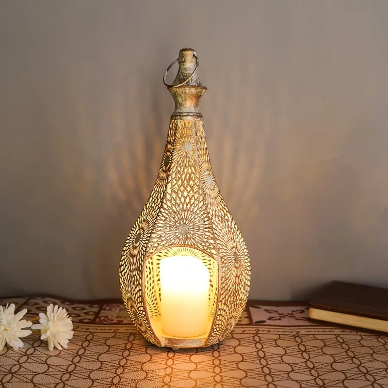 Moroccan-style teardrop iron hanging lantern in distressed gold with intricate hollow floral patterns and a glowing candle.