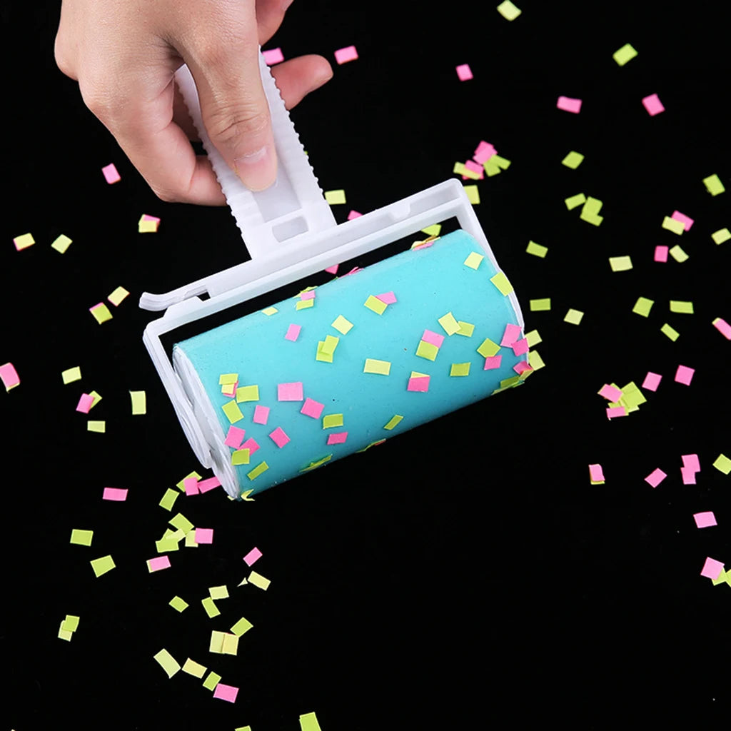 Hand holding a white lint roller with a blue adhesive sheet covered in small pink and yellow confetti.
