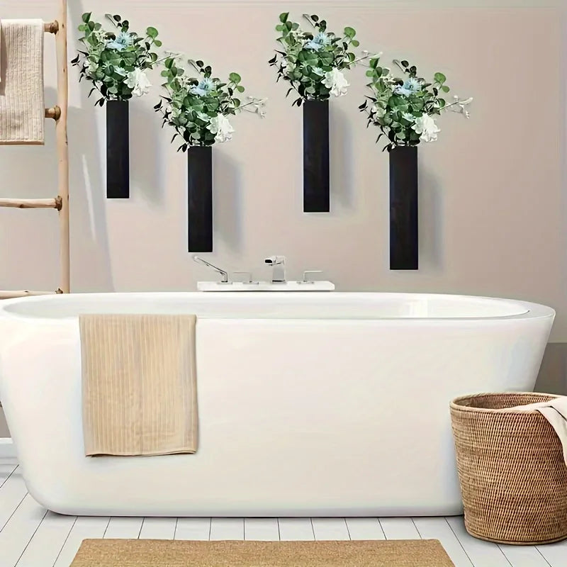 Four sleek, black rectangular wall-mounted vases filled with lush green foliage, displayed above a white bathtub.